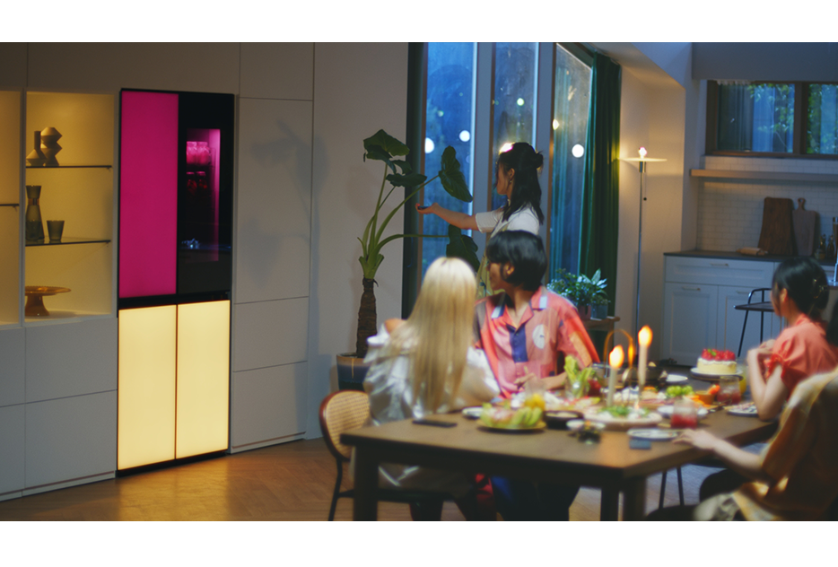 A woman is remotely playing music via a built-in Bluetooth speaker of the LG MoodUPTM refrigerator at the house party