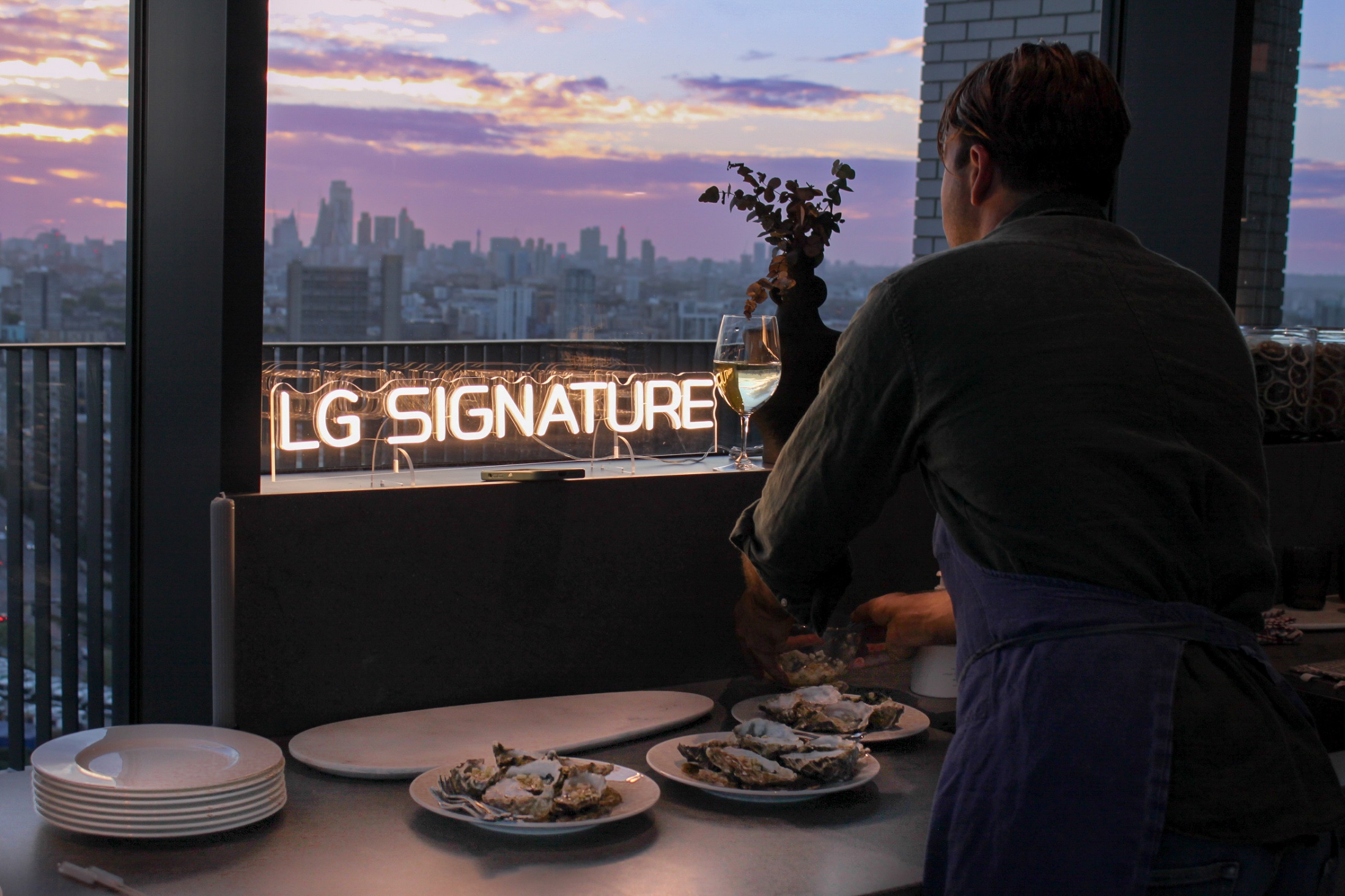 A chef preparing food as he looks out on to the London skyline and “LG SIGNATURE” neon sign