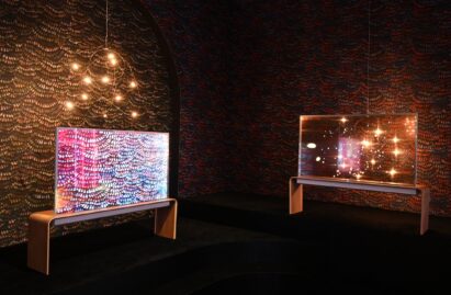 Two of LG’s newly unveiled LG Transparent OLED model displayed in a dark room with bright lights, one transparent and the other displaying content.