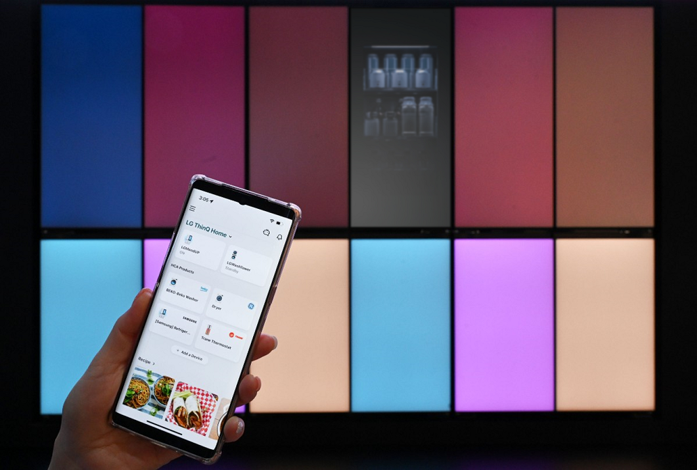 LG MoodUP fridges are exhibited at CES 2023 while a smartphone on the left side of the image displays LG ThinQ app