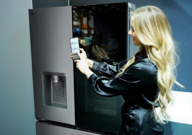 A woman is showing the LG ThinQ app on a smartphone in front of the InstaView fridge at the Kitchen and Bath Industry Show 2023