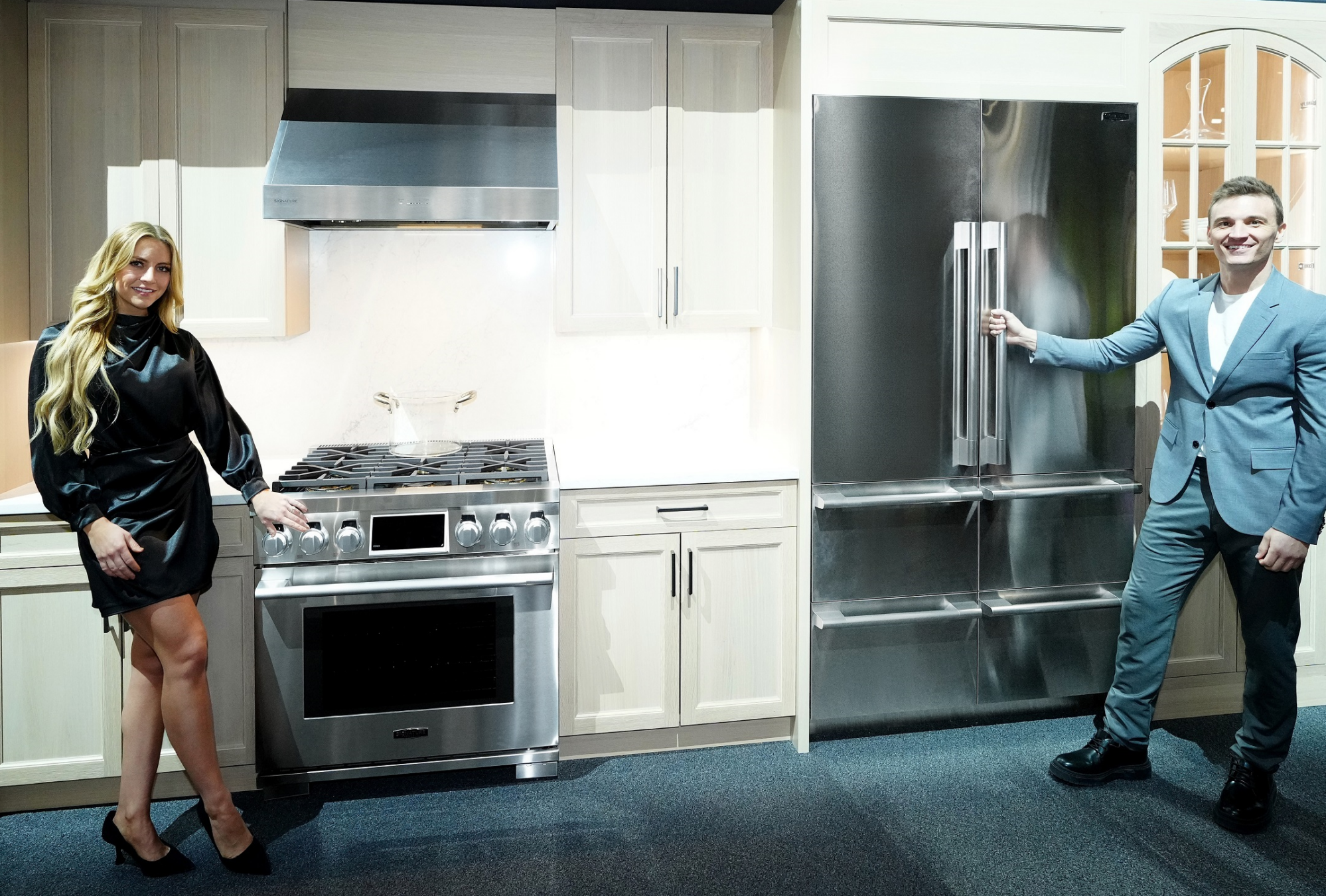 A woman and a man are standing beside the Signature Kitchen Suite 36-inch Dual-Fuel Pro Range and 48-inch French-Door fridge in the LG booth at Kitchen and Bath Industry Show 2023