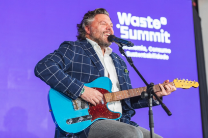 Comedian César Mourão playing a guitar and singing on stage during the Waste Summit.