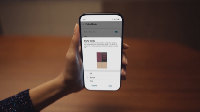 A hand holding a smartphone displaying the MoodUP fridge Party Mode image in the ThinQ app
