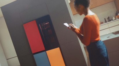 A woman on the right holding her smartphone and standing in front of the MoodUP fridge