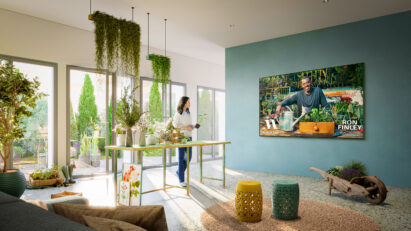 A woman watching a gardening lesson from the MasterClass app on her wall-mounted LG Smart TV as she tends to her plants