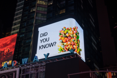 A close-up photo of a billboard in Times Square, New York displaying a bunch of vegetables with a phrase 