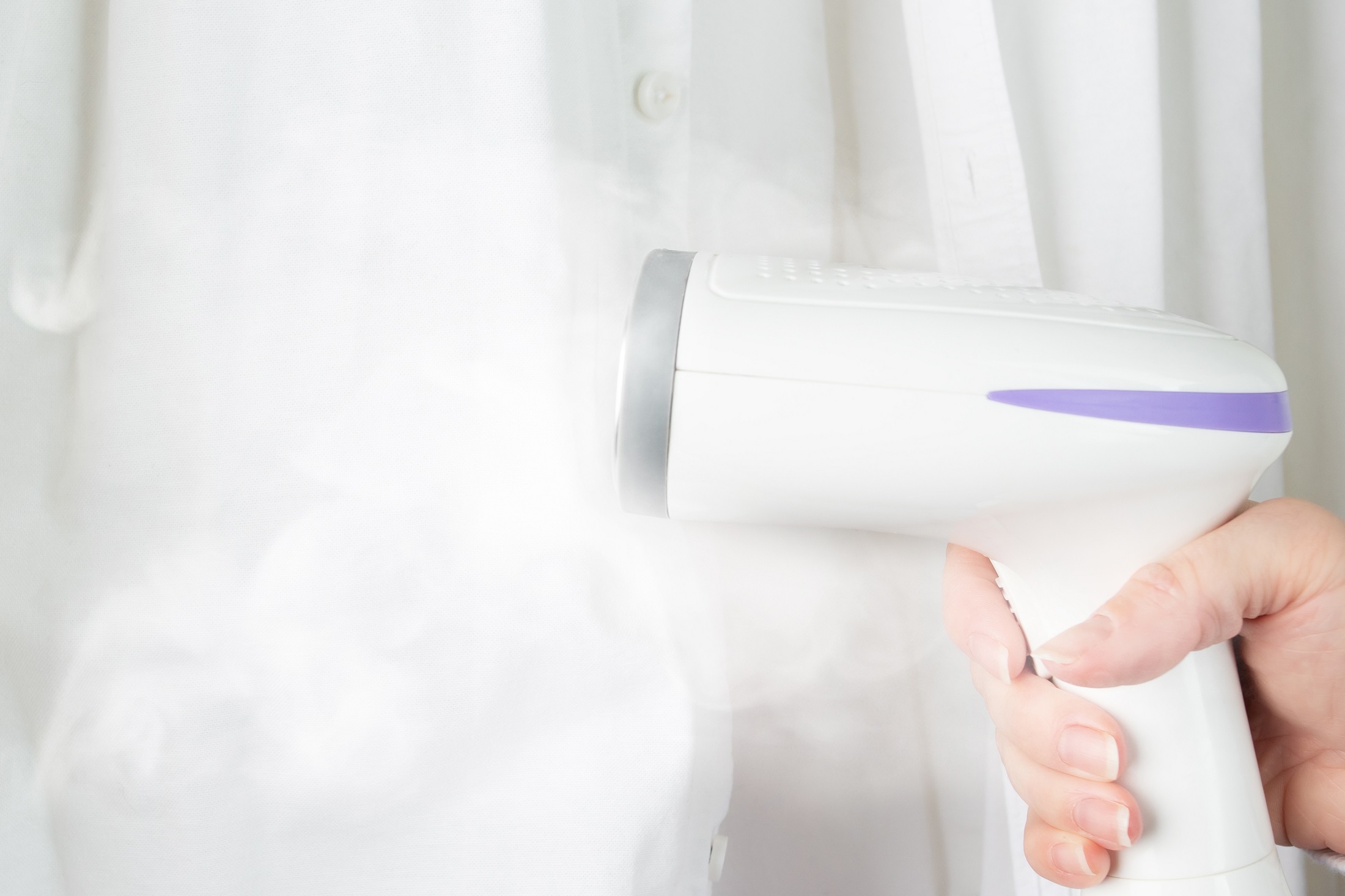 A photo of a human handing using a steamer to get rid off wrinkle on a white shirt