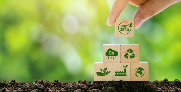 A human hand placing a wooden block that reads 'NET ZERO' on the top of bunch of blocks