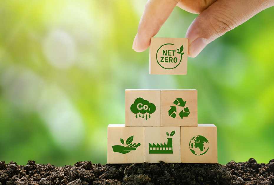 A human hand placing a wooden block that reads 'NET ZERO' on the top of bunch of blocks