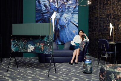 A woman watches LG OLED Objet Collection Posé next to LG XBOOM 360 portable speaker, which both sport an artistic design by Dutch brand Moooi, as she sits in a room full of artwork