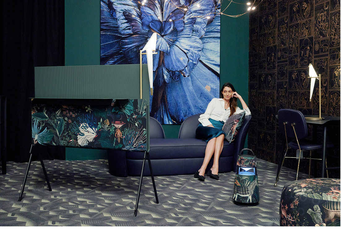 A woman watches LG OLED Objet Collection Posé next to LG XBOOM 360 portable speaker, which both sport an artistic design by Dutch brand Moooi, as she sits in a room full of artwork