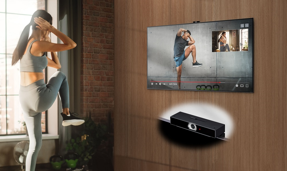 A woman using a fitness application on her LG TV to exercise at home, with LG Smart Cam attached to the top of the TV