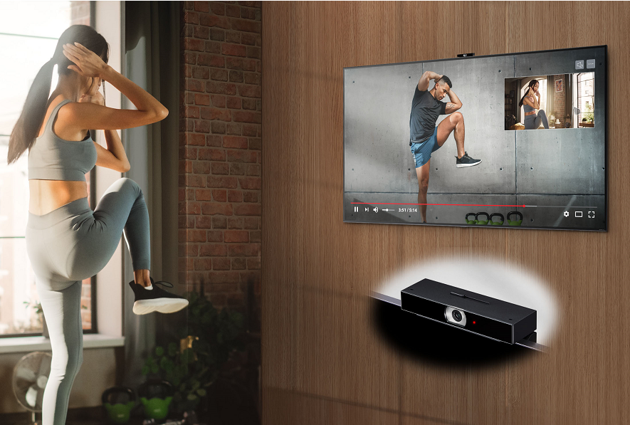 A woman using a fitness application on her LG TV to exercise at home, with LG Smart Cam attached to the top of the TV