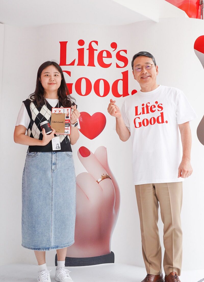 LG CEO posing with LG employee in front of the white wall decorated with a phrase "Life's Good"