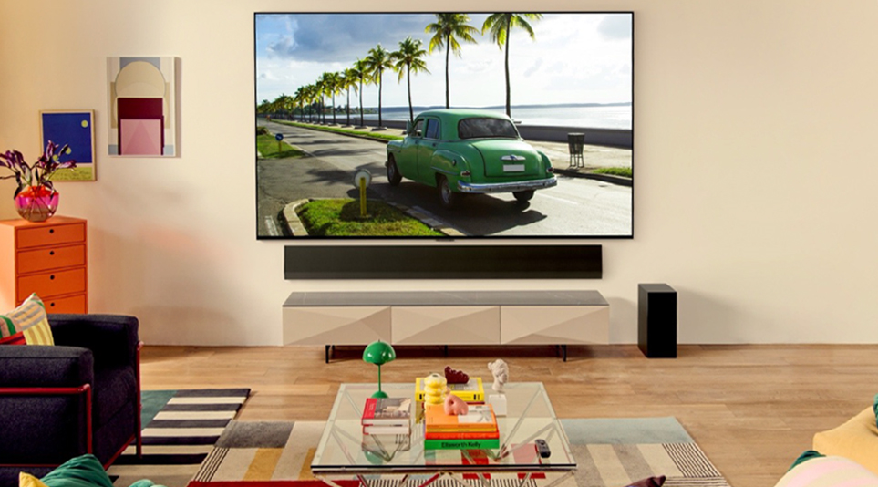 LG OLED TV in a bright living room displaying a green car driving down a road by the beach
