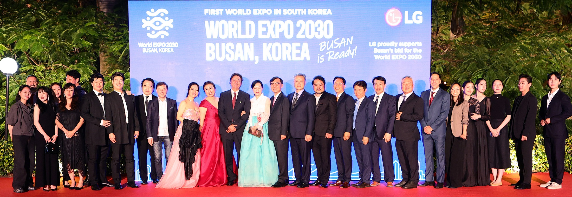 A photo of opera-related actors and staff posing on the podium with a digital screen at the back displaying the phrase "WORLD EXPO 2030 BUSAN, KOREA"