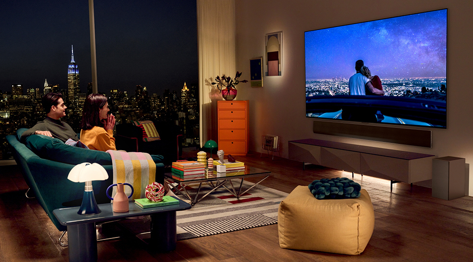 A couple watching a romantic movie on their LG OLED TV in a modern living room overlooking the New York City skyline at night