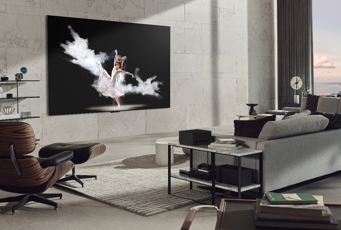 A wall-mounted LG SIGNATURE OLED M3 model displays an image of a woman performing ballet in a modern, gray-toned living room