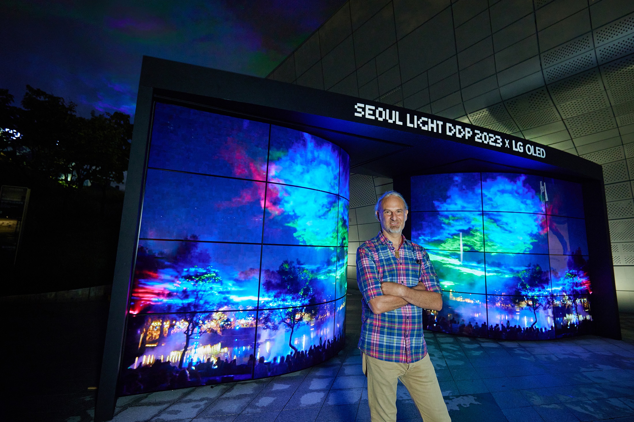 Artist Dan Archer standing in front of the Seoul Light DDP 2023 with numerous panels displaying his vibrant artwork
