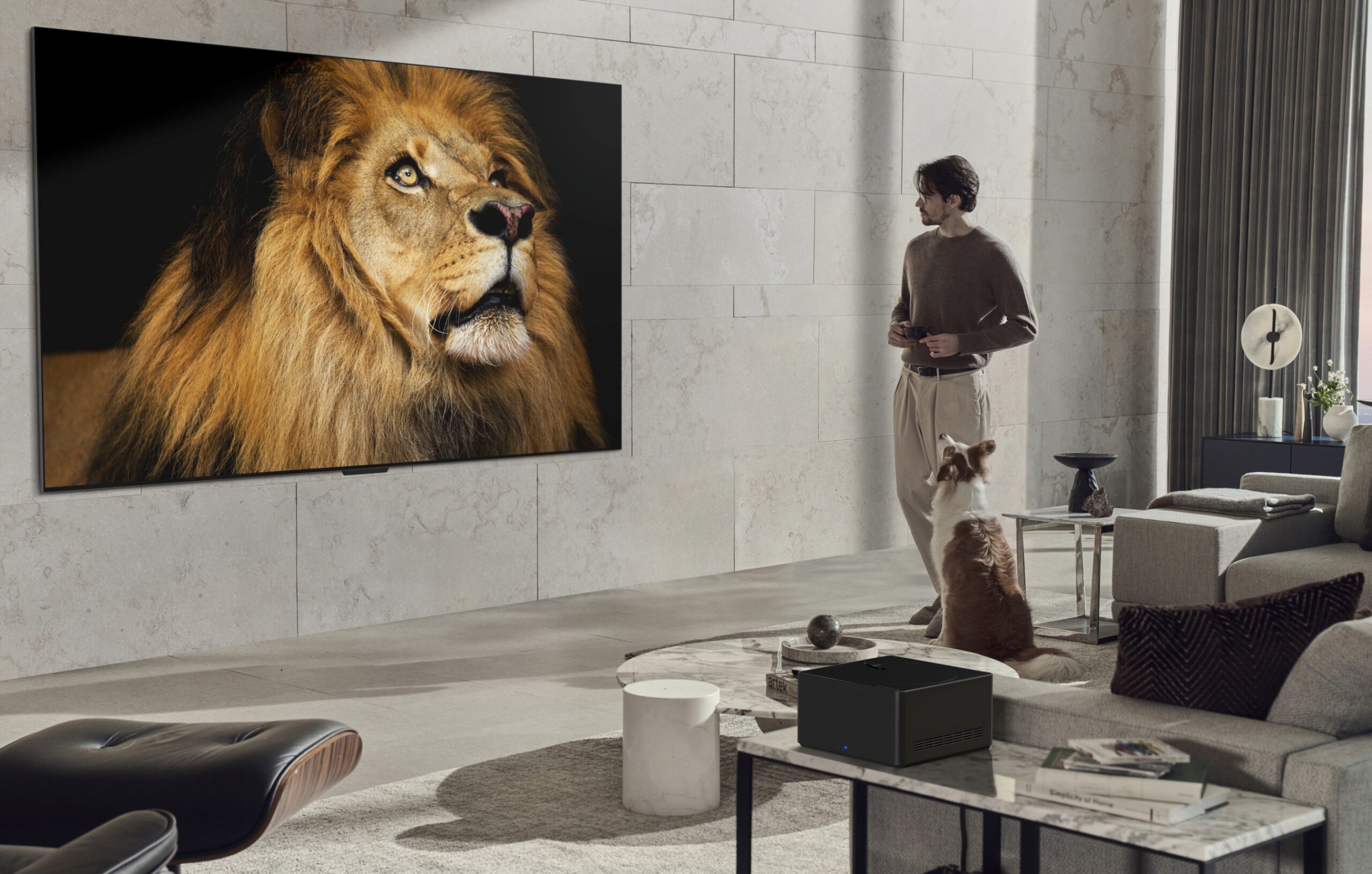 A man stands in a gray living room, looking at the LG SIGNATURE OLED M3 model mounted on the wall