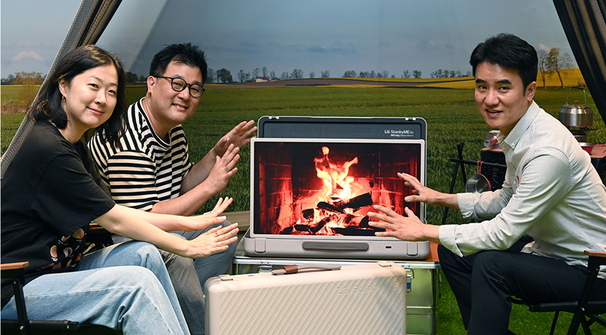 Three LG representatives sitting around a display of a campfire on the LG StanbyME Go model