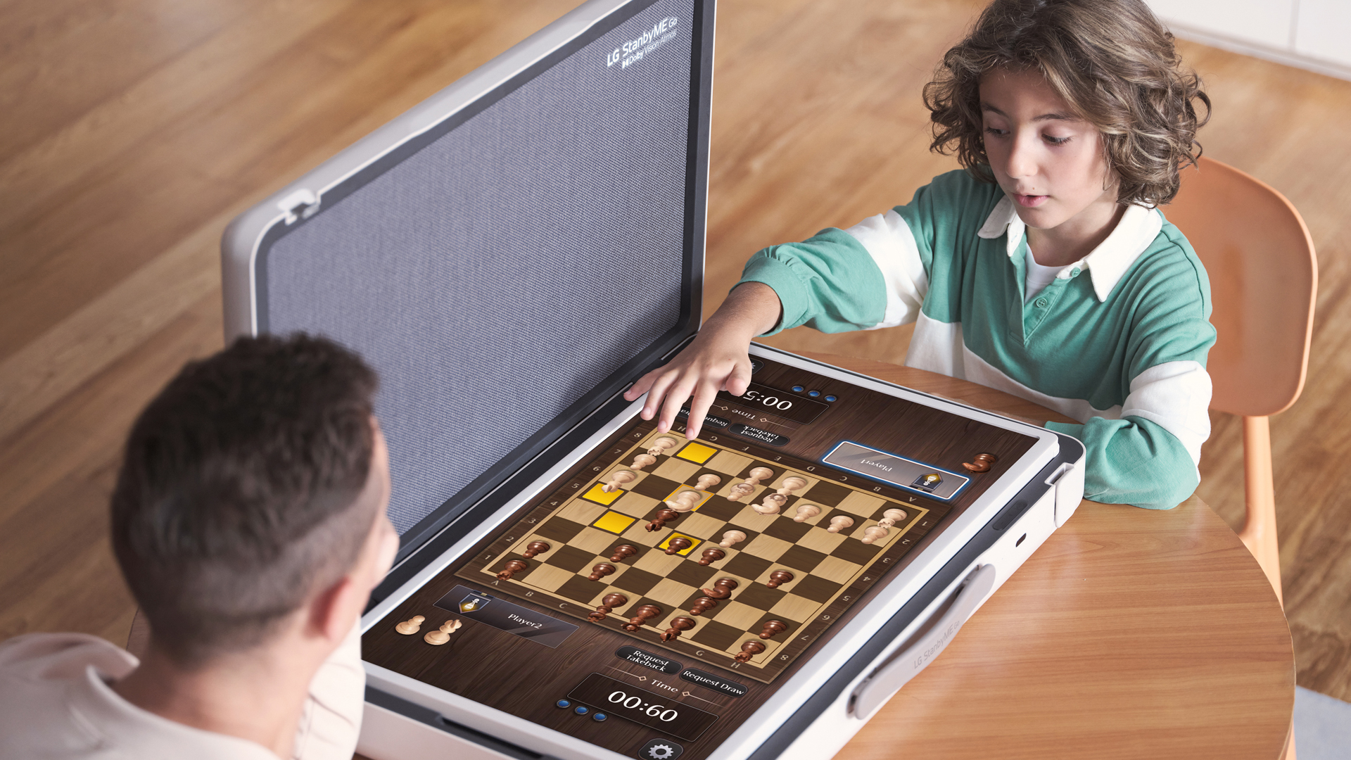 A father and son play a game of chess game at a desk using the LG StanbyME Go model in table mode.