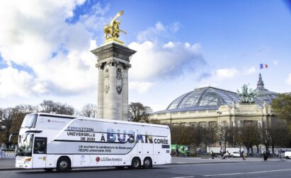 A photo of a big LG Bus with the words 'A Busan Coree' passing by the city