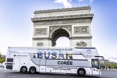 A photo of a big LG Bus with the words 'A Busan Coree' passing by the center of Arc de Triomphe