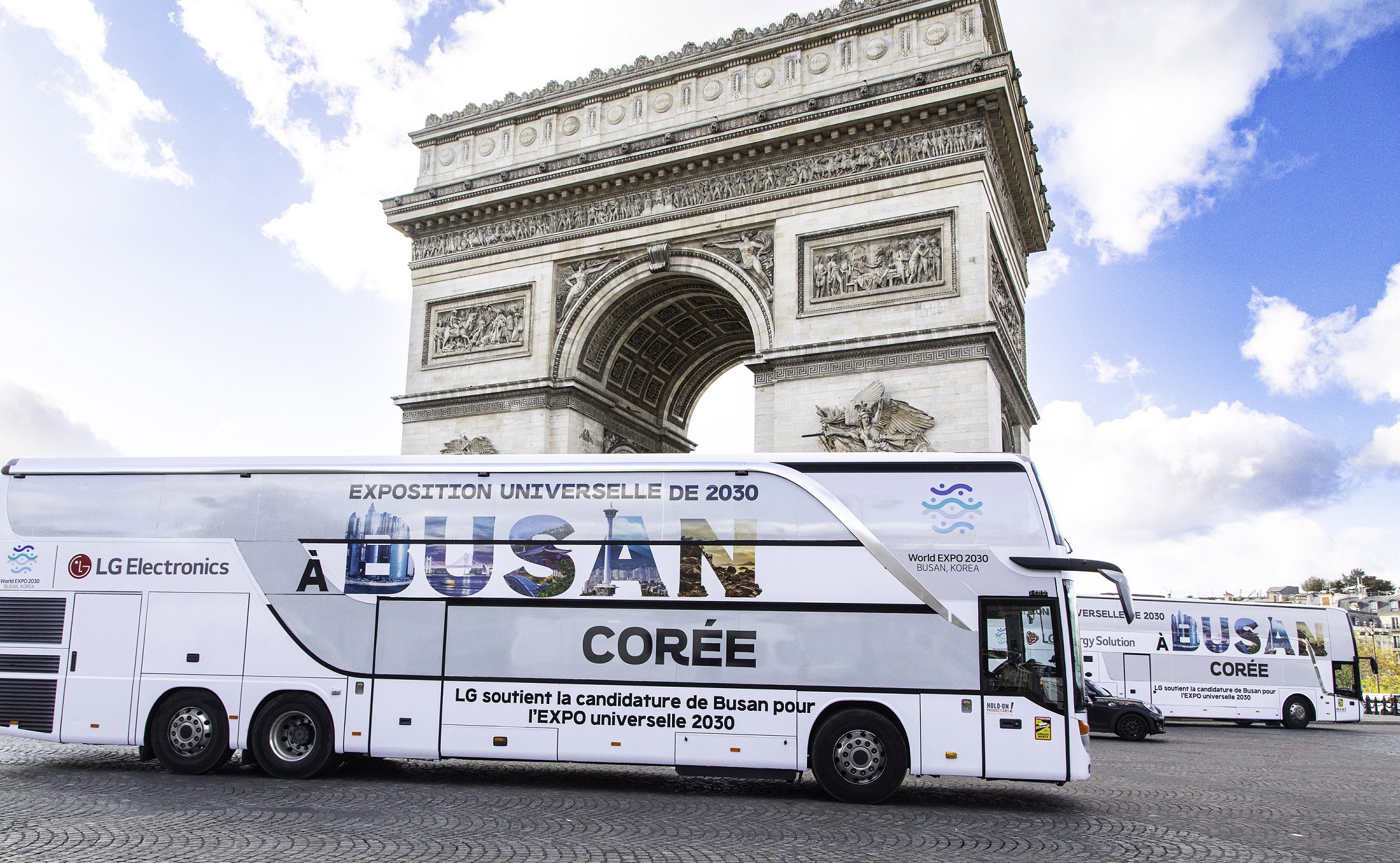 A photo of a big LG bus with the words 'A Busan Coree' passing by Arc de Triomphe