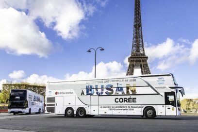 A photo of a big LG bus with the words 'A Busan Coree' passing by the Eiffel Tower
