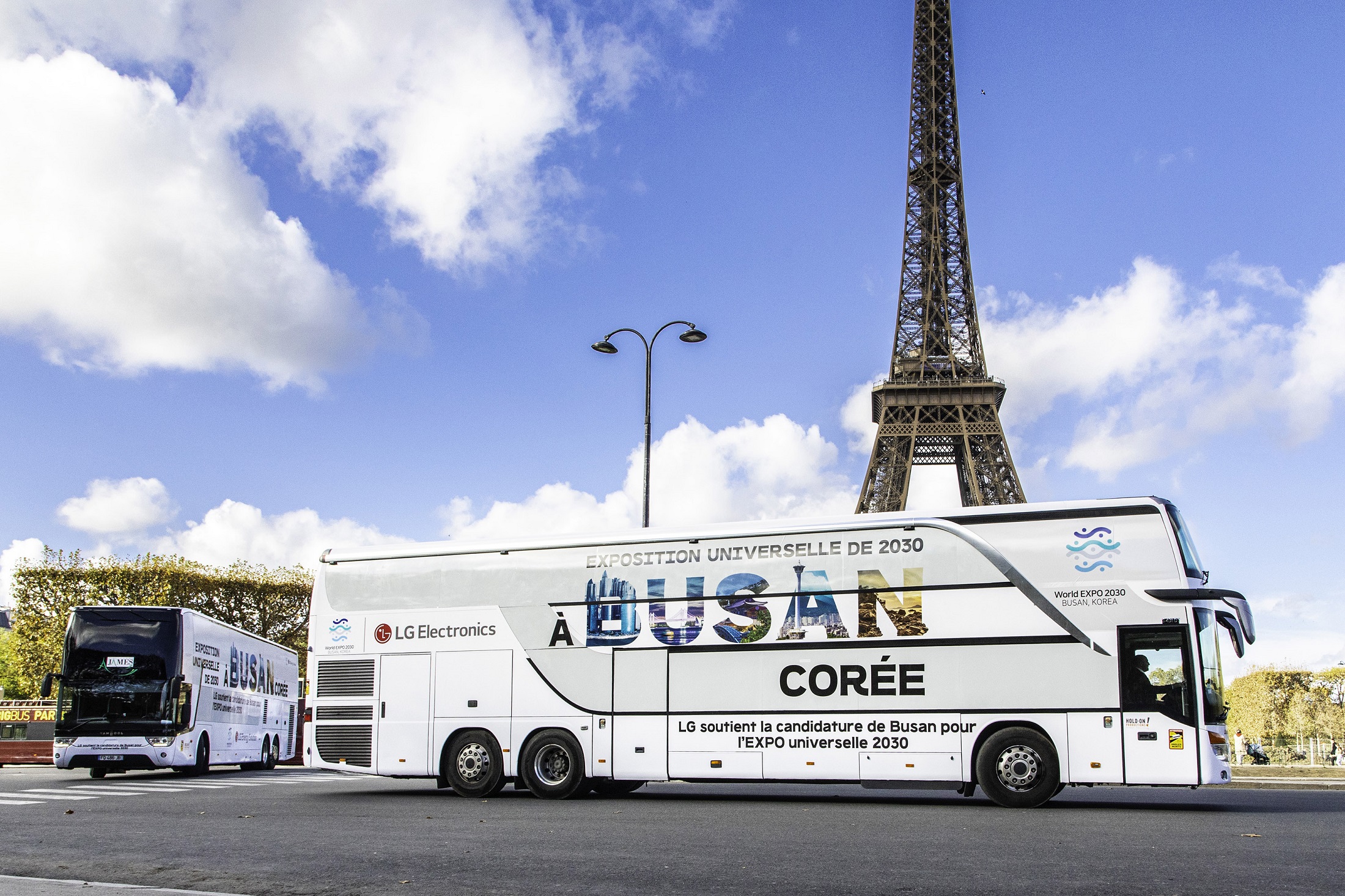 A photo of a big LG bus with the words 'A Busan Coree' passing by the Eiffel Tower