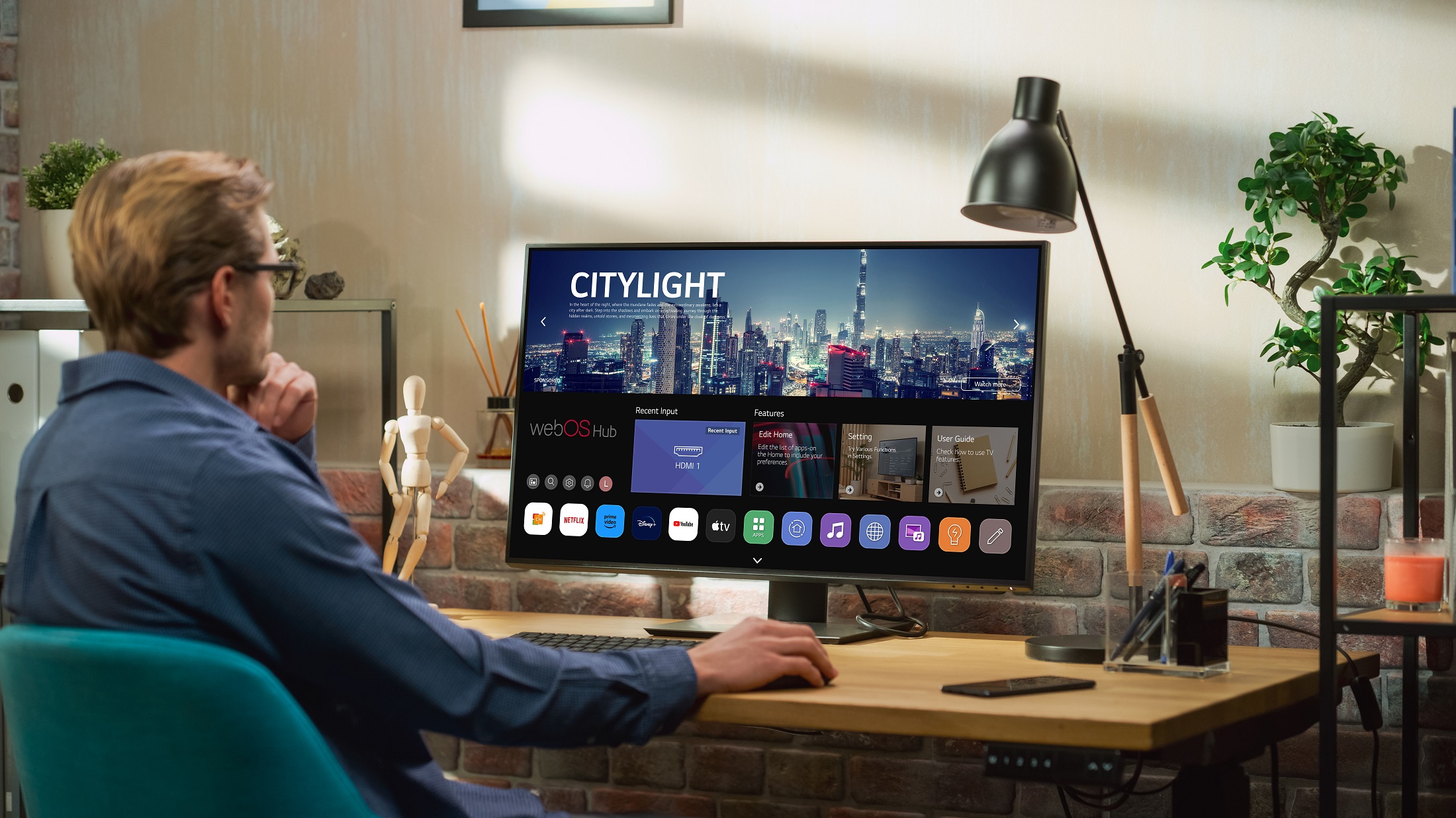 A man sitting at a desk explores the home UI of the new webOS Hub 2.0S on an LG smart monitor