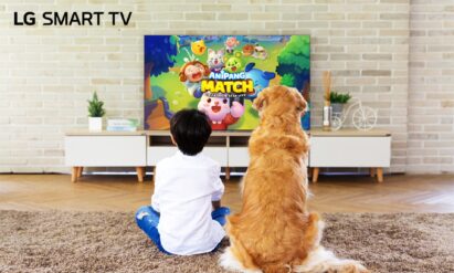 A boy and his golden retriever sitting on a living room carpet in front of an LG Smart TV, about to play Anipang Match