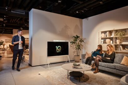 Two people sitting on a couch and one person standing next to the LG Objet Collection Pose
