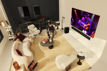 A couple relaxes in a living room, watching a band play on a wall-mounted LG OLED evo G4