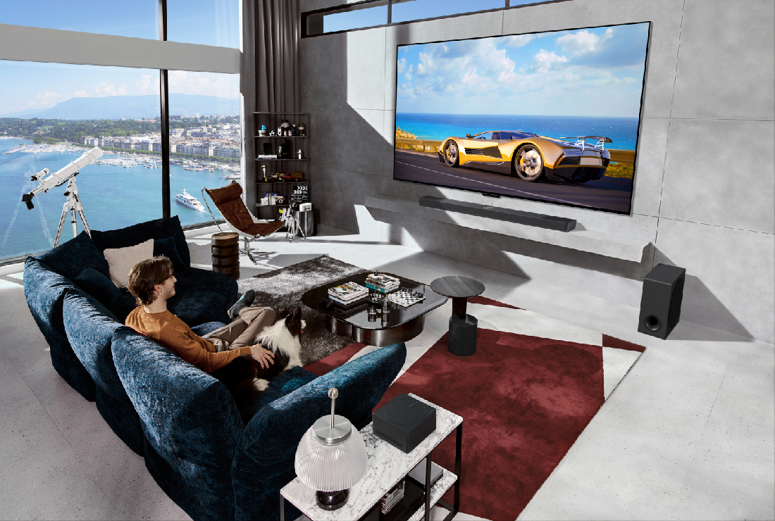 Car displayed on a wall-mounted LG OLED evo M4 captures the attention of a man and his border collie