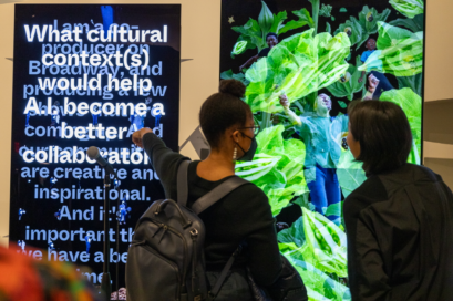 Two women are discussing Dinkin’s artwork, pointing to a screen that reads 