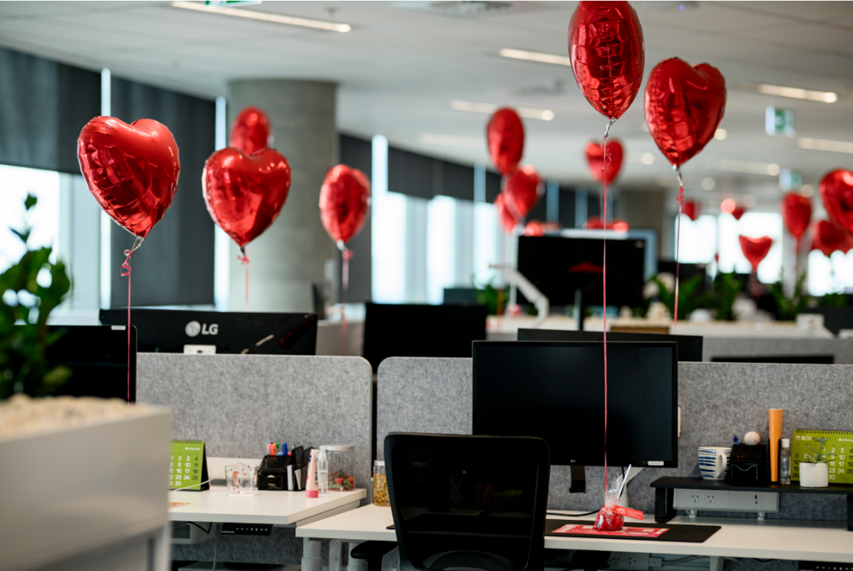 A photo of red heart balloons attached to workers' desks 