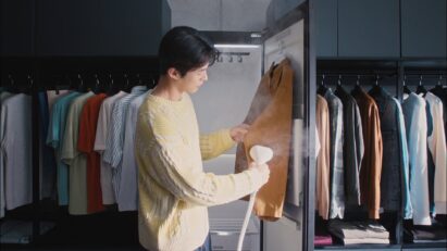 A photo of a man using a handheld high-pressure steamer attached to the LG Styler on a shirt in a dressing room