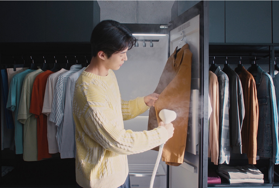 Photo of a man using a handheld high-pressure steamer attached to the LG Styler on a shirt in a dressing room