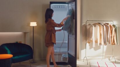 A photo of a women using a handheld high-pressure steamer attached to the LG Styler on a shirt in a dressing room.