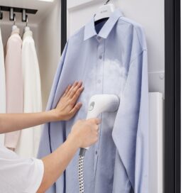A photo of a person using a handheld high-pressure steamer on a shirt inside the LG Styler door