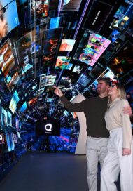 A man and a woman are pointing at the large variety of content playing throughout the LG webOS zone