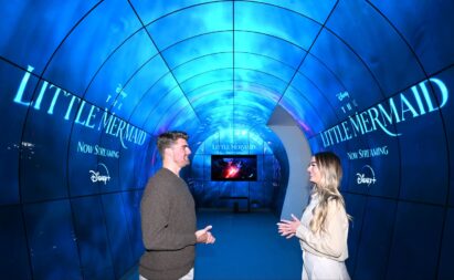 A man and a woman are standing in the middle of the webOS zone, having a conversation while surrounded by the title screen of ‘The Little Mermaid,’ streaming on Disney+