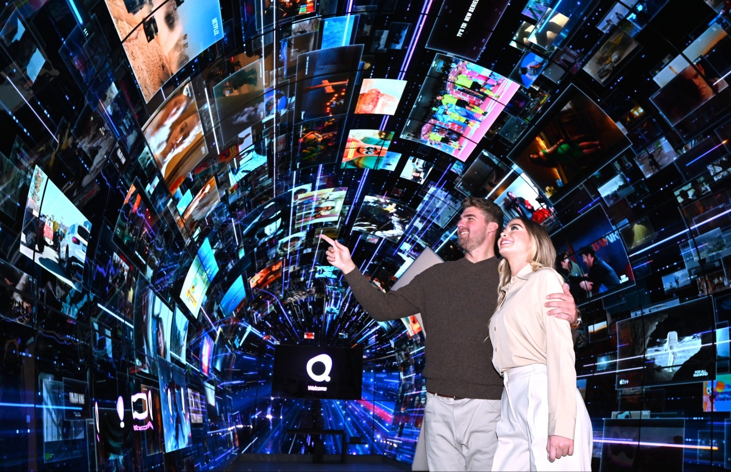 A man and a woman are pointing at the large variety of content playing throughout the LG webOS zone