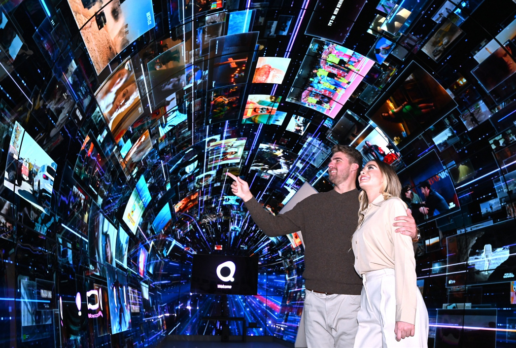 Man and a woman are pointing at the large variety of content playing throughout the LG webOS zone