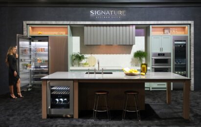 Front view of a woman standing by the refrigerator in the Signature Kitchen Suite zone at KBIS 2024