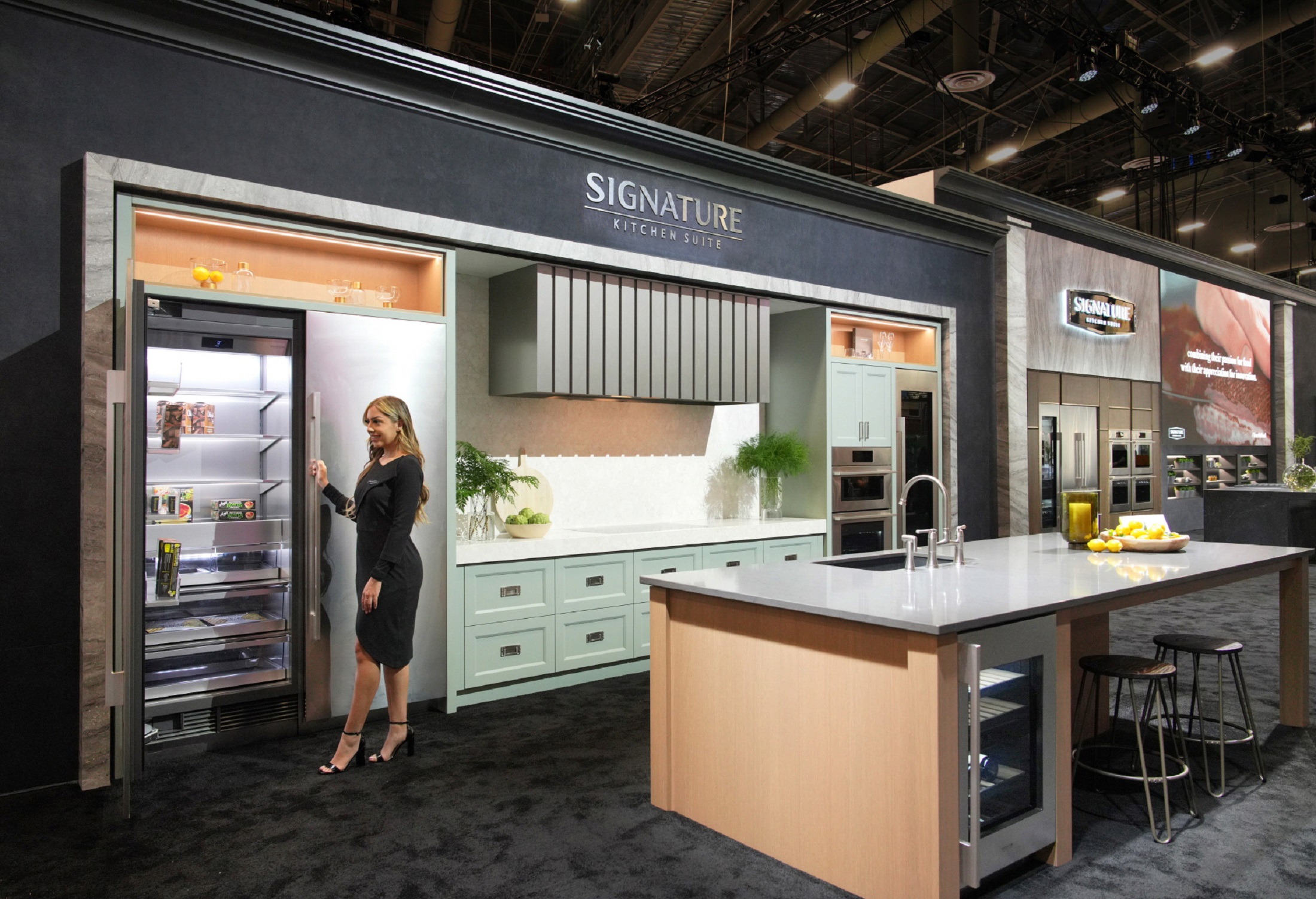 A photo of a woman standing by the refrigerator in the Signature Kitchen Suite zone at KBIS 2024