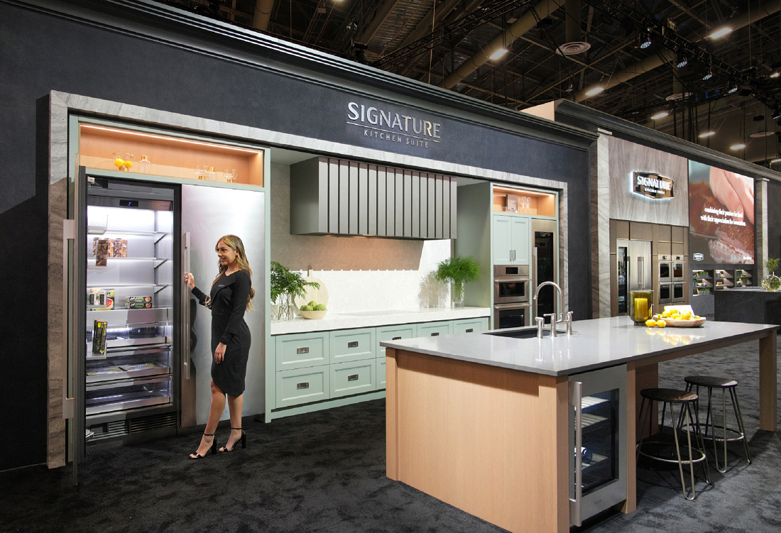 An image of a woman standing by the refrigerator in the Signature Kitchen Suite zone at KBIS 2024